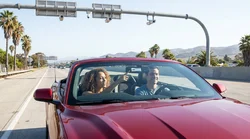 A silver car rental driving along a sunny California highway under an electronic toll sign