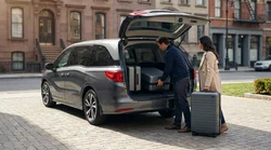 Person loading three large suitcases into the open trunk of a car rental on a New York street