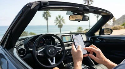 Driver holding a smartphone with map navigation inside a car rental on a scenic highway in California