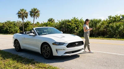Man looking under the hood of a broken down car rental on a sunny Florida highway