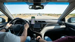 Smartphone on a dashboard mount showing GPS navigation inside a car rental on a Texas highway