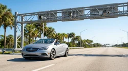 A white car rental passing under an electronic toll gantry on a sunny Florida highway