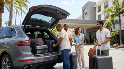 Four adults loading luggage into the trunk of a spacious car rental in Los Angeles