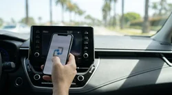 Driver holding a smartphone near the dashboard screen of a car rental in California