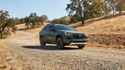 Silver car rental driving on a dusty gravel road surrounded by dry brush in a sunny California landscape