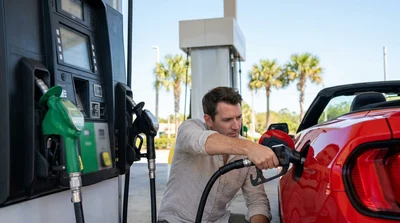 Person inserting a fuel pump nozzle into a car rental at a sunny gas station in Florida