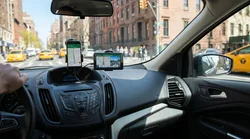 Driver checking a phone navigation screen on the dashboard of a car rental driving down a busy New York street