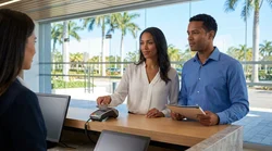 A customer hands a credit card to a car hire agent across a service desk in Miami