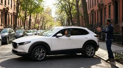 Small silver car rental parallel parked on a crowded New York street surrounded by tall brick buildings