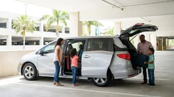 Family loading luggage into a white 7-seater car rental parked outside the Orlando airport