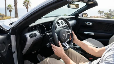 Portable hand controls attached to the steering wheel of a car rental parked on a scenic California coastal road