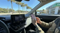 Person holding a smartphone near a car dashboard screen inside an Orlando car rental