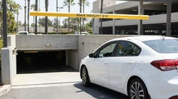 White car rental passing under a yellow low-clearance sign at a parking garage in California