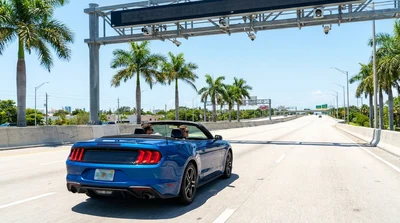 White car rental driving under an electronic toll gantry on a sunny highway in Miami