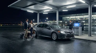 Row of parked cars under bright lights at a New York airport car rental lot at night
