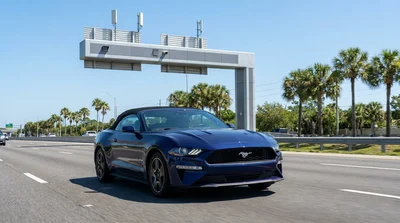 White car rental vehicle passing under a SunPass toll gantry on a sunny highway in Florida