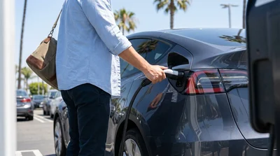 White Tesla electric car rental connected to a charging station along a sunny street in California