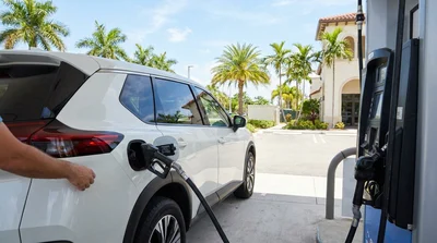 Person pumping gas into a white car rental at a sunny gas station in Miami