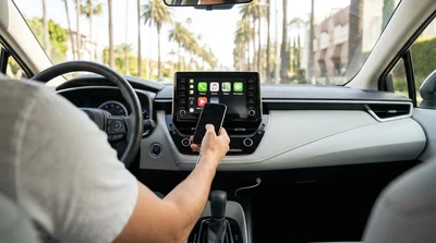 Dashboard screen showing Apple CarPlay inside a car rental parked near palm trees in Los Angeles