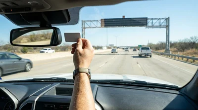 Dashboard view from a car rental approaching an overhead toll gantry on a Texas highway