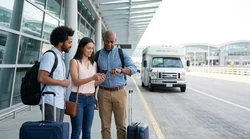 White shuttle bus with a car rental sign picking up passengers outside a New York airport terminal