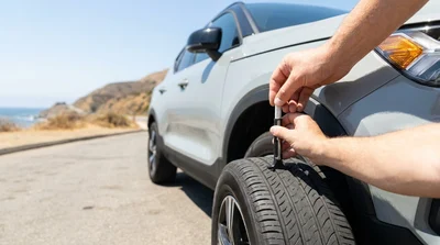 Close up of a person checking the tyre tread on a car rental parked along a sunny California highway
