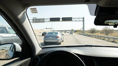 White car rental passing under an electronic toll gantry on a bright highway in Texas