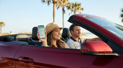 Smartphone displaying a map app mounted on the dashboard of a car rental driving on a sunny Florida highway