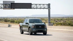 Silver car hire driving under an overhead electronic toll gantry on a sunny Texas highway
