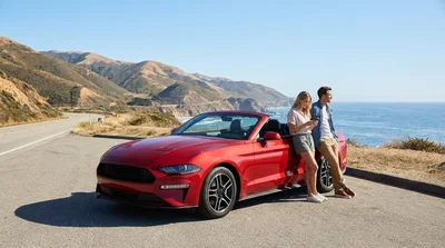Driver checking the engine of a broken-down car rental on the shoulder of a California highway