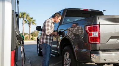 Driver pumping fuel into a white car rental at a gas station in Texas