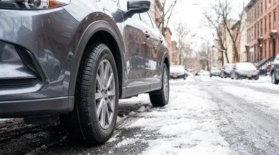 Silver car rental with winter tires driving through deep snow on a New York street