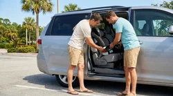 A parent installing a child safety seat in the back of a white Orlando car rental