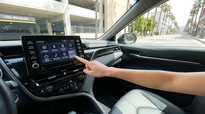 Driver touching the dashboard screen of a car rental parked on a sunny Los Angeles street