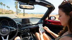 Smartphone displaying GPS navigation on the dashboard of a car hire driving on a sunny California highway