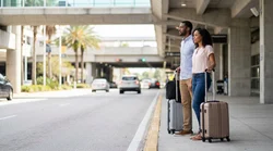 Passengers with luggage boarding a shuttle bus outside the Orlando airport terminal for a car rental