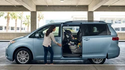 Father securing a child seat in the back of a car rental parked on a bright California street