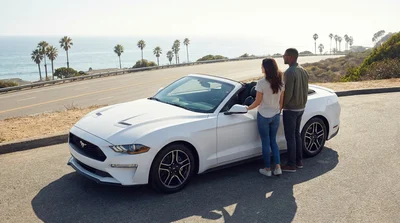 Couple driving a convertible car rental along a sunny coastal road in California