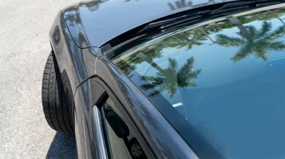 Close up of the windscreen and front tire of a white car rental parked along a sunny Florida beach