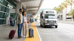 Travelers with luggage waiting for a car hire shuttle bus outside Terminal 2 in Los Angeles