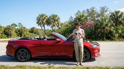 Driver looking under the hood of a broken-down car rental on a sunny Florida road