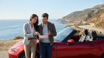 Red car rental driving along a scenic coastal highway in California overlooking the ocean