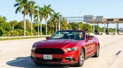 Silver car rental driving on a sunny Florida highway approaching a toll plaza