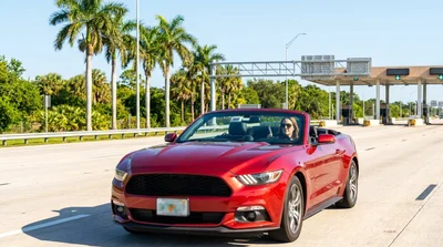 Silver car rental driving on a sunny Florida highway approaching a toll plaza