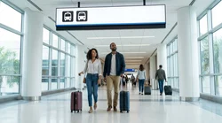 Travelers with luggage walking past an overhead sign for the car rental center inside a Miami airport terminal