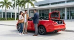Man loading luggage into a white car rental parked near palm trees in sunny Florida