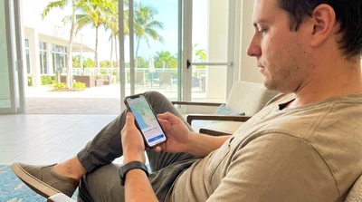 Person checking a smartphone map outside a Florida car rental agency with palm trees