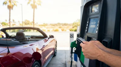 Driver holding a fuel pump nozzle to fill up a white car rental at a gas station in California
