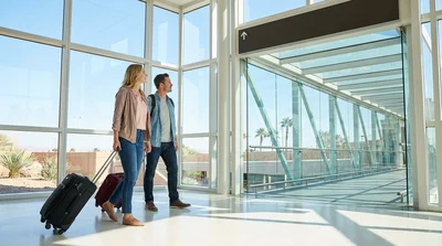 Travelers rolling luggage through the Las Vegas airport terminal toward the car hire center