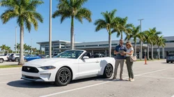 Person driving a silver car hire on a sunny coastal road with palm trees in Florida